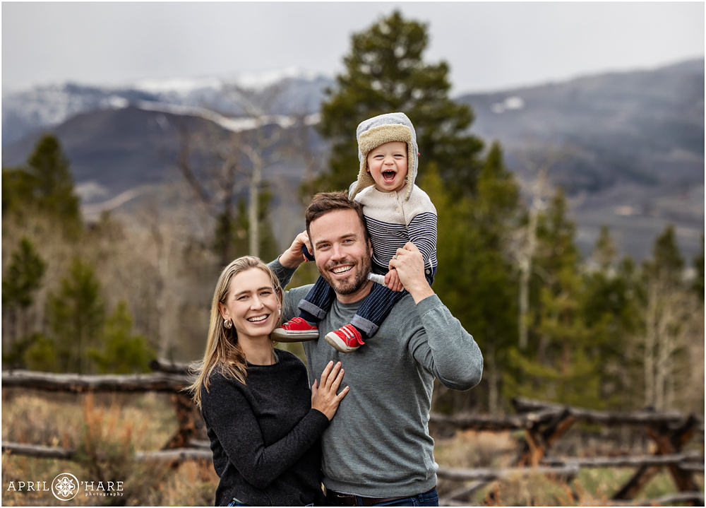 Cute family photo for a family of 3 with a young son wearing a trapper style hat sitting on his dad's shoulders at Granby Ranch in Colorado