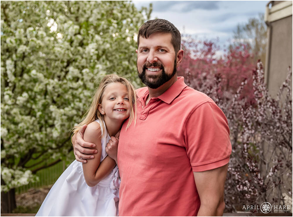 First communion portrait for a girl with her dad in their backyard on a stormy spring day with spring blossom backdrop