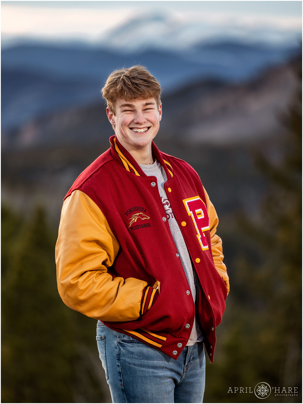 High School Senior Boy wearing a Ponderosa High School Mustangs Letter Jacket in Red and Yellow with Blue Mountain Backdrop in Evergreen Colorado