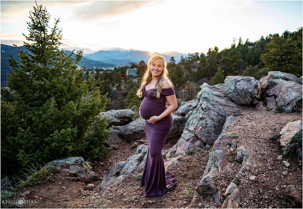 Maternity portrait for a woman with long blonde hair and a form fitting lilac colored dress at West Mount Falcon in Colorado