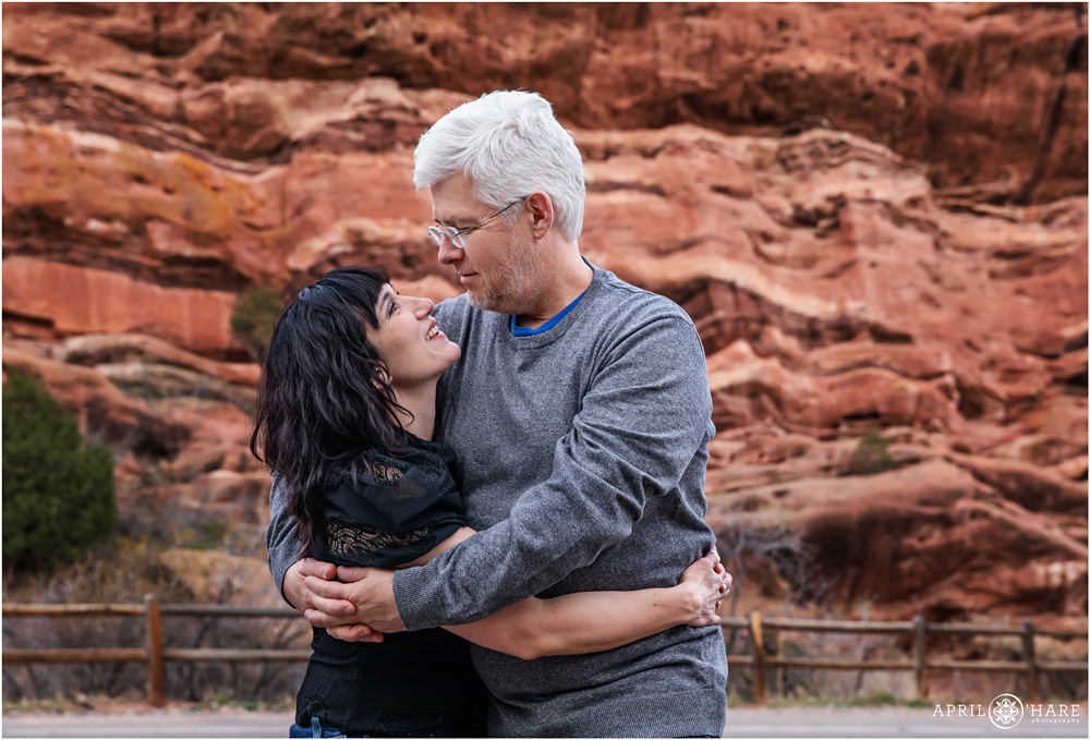 Couple looks into each others eyes and smiles in front of a beautiful red rocks formation at the Amphitheater in Morrison, CO