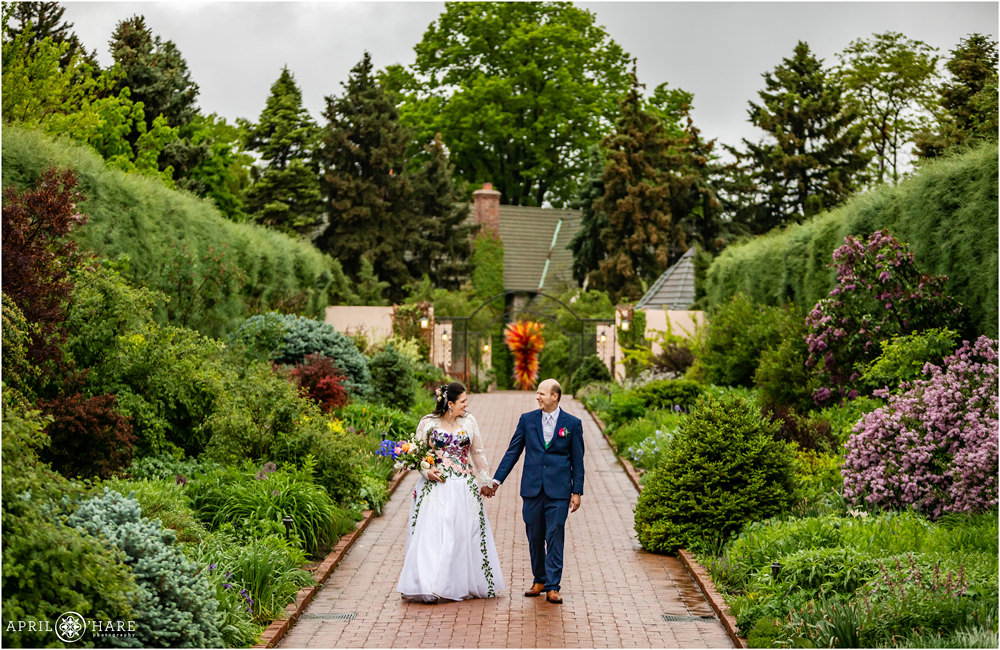 Dramatic garden filled walkway with bride and groom hand in hand at Denver Botanic Gardens on a stormy wedding day
