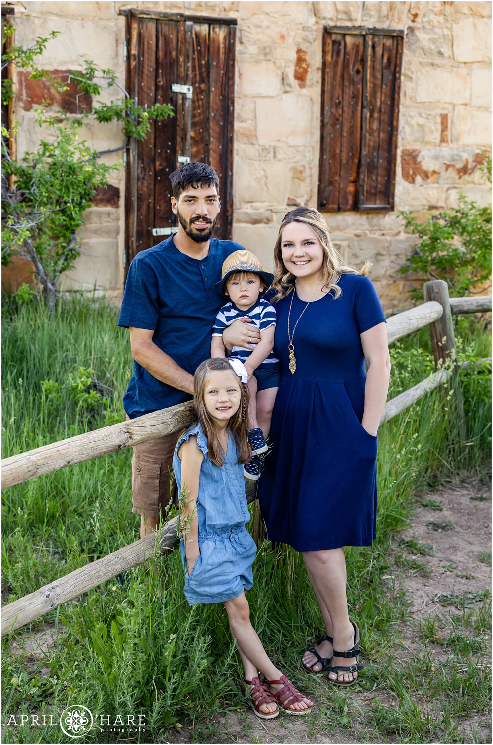 Cute family of 4 pose in front of the historic stone house at South Mesa Trail in Boulder Colorado
