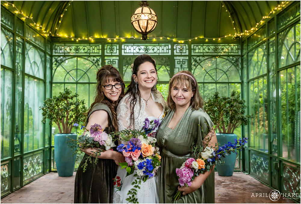 Bride with her maid and matron of honor inside the green solarium on a wet and rainy wedding day at Denver Botanic Gardens