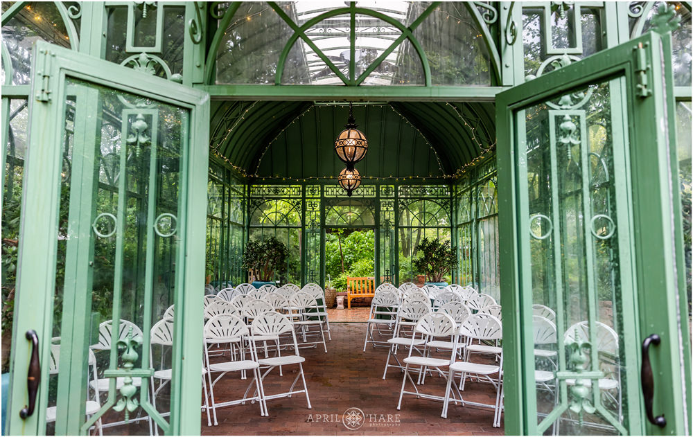 View of the Denver Botanic Gardens green solarium set up for wedding ceremony from the outside looking in with doors open on one end