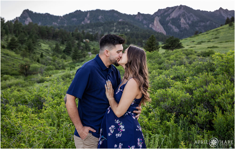 A young couple expecting their first baby kiss in front of a pretty mountain backdrop at South Mesa Trail in Boulder Colorado