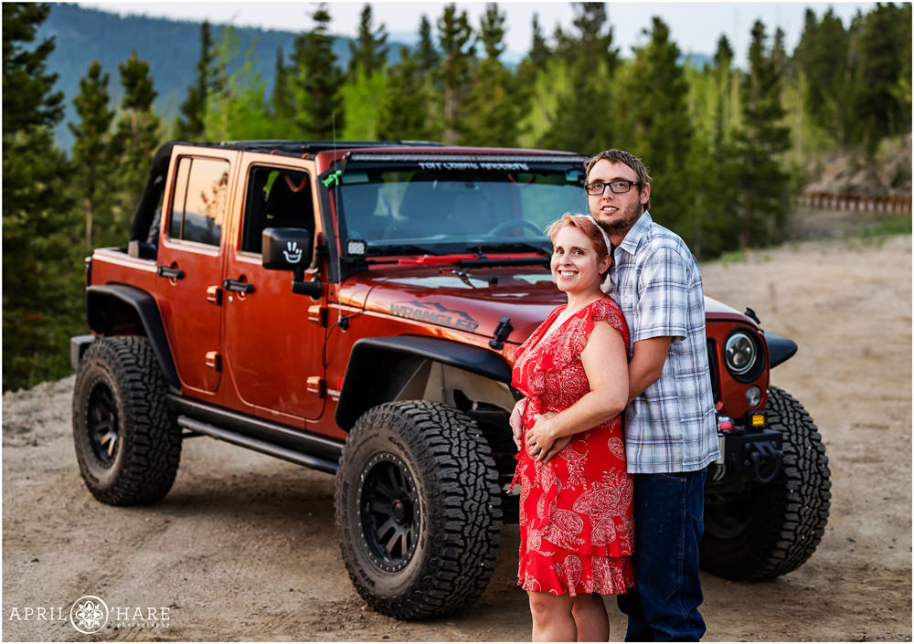 Couple pose for an engagement photo in front of their red Jeep Wrangler in the mountains of Colorado