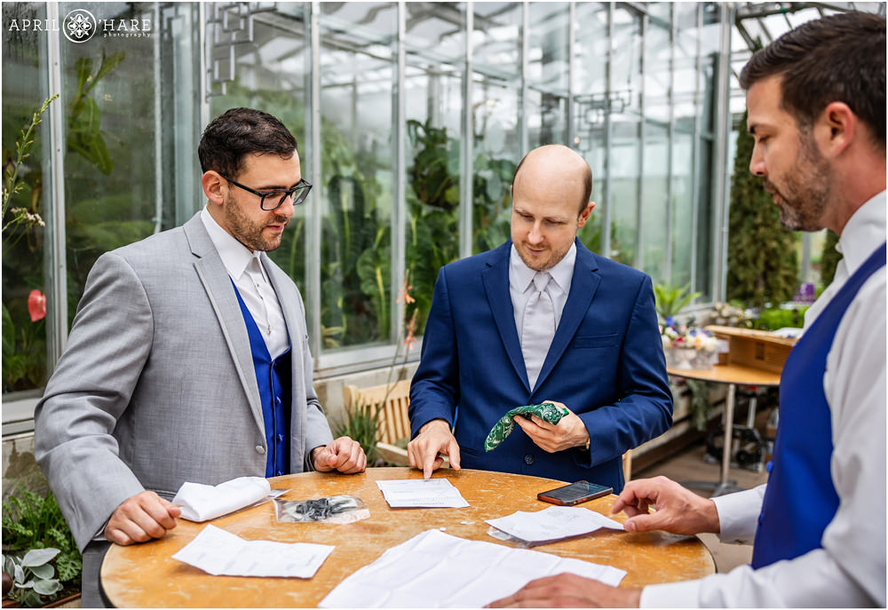 Groom with his groomsmen getting folding their pocket squares with instructions on table inside the Orangery at Denver Botanic Gardens