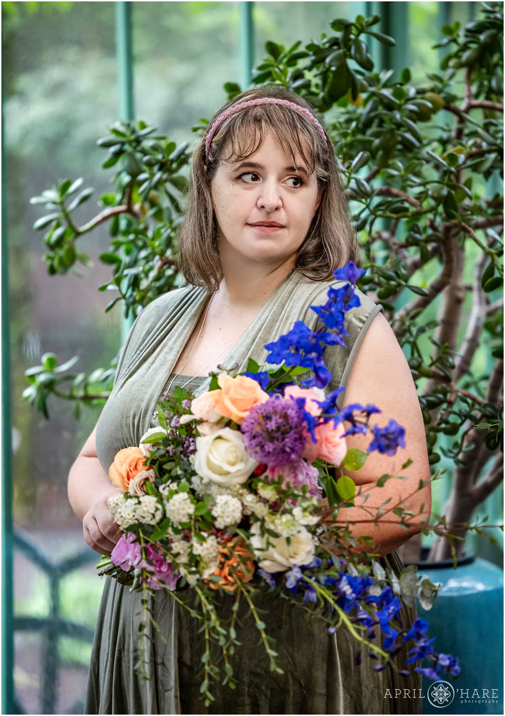 Matron of honor looks out at guests while standing in front of a Jade plant inside the Green Solarium at her friend's rainy wedding day at Denver Botanic Gardens