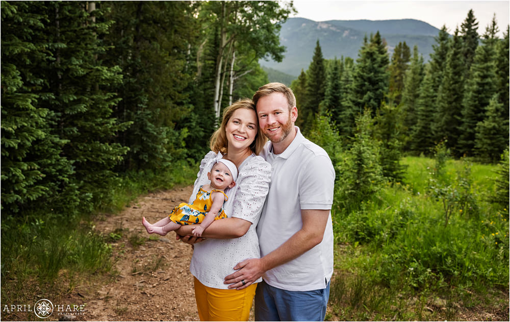 Family wearing white blue and yellow pose for a family picture with their new 3 month old baby girl in Evergreen Colorado