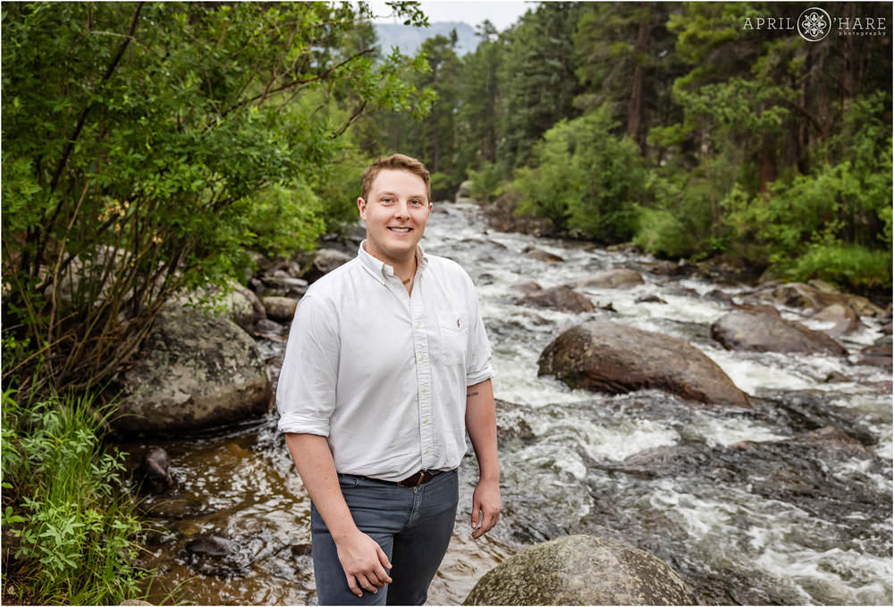 Young man wearing a white button up shirt poses in front of the beautiful Big Thompson River inside Rocky Mountain National Park in Colorado