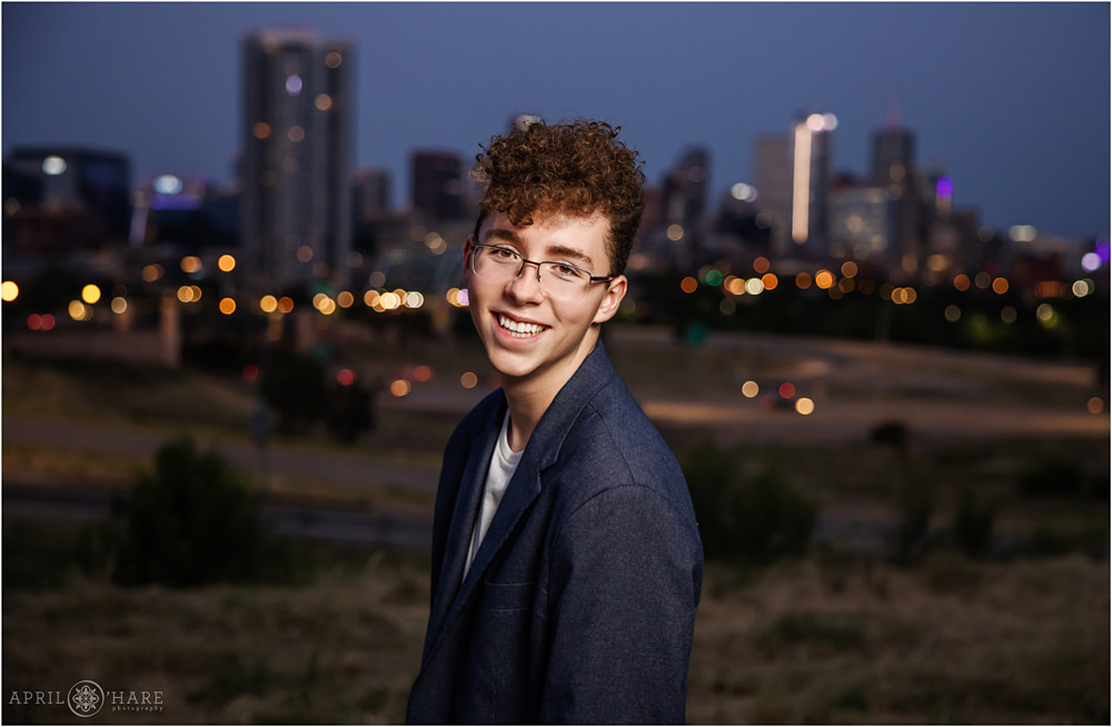 High school senior boy photographed in front of Denver skyline at dusk