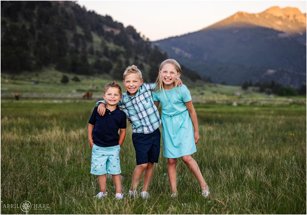 Sweet photo of 3 young siblings laughing together at Rocky Mountain National Park with elk in the backdrop