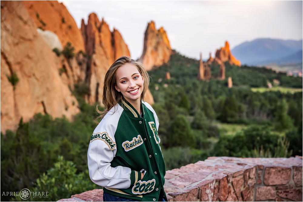 A high school senior girl wearing a green and white letter jacket at Garden of the Gods in Colorado Springs