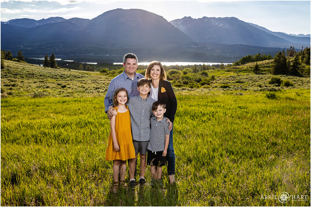 A family of 5 with 3 children pose in a mountain field on a sunny day near Breckenridge