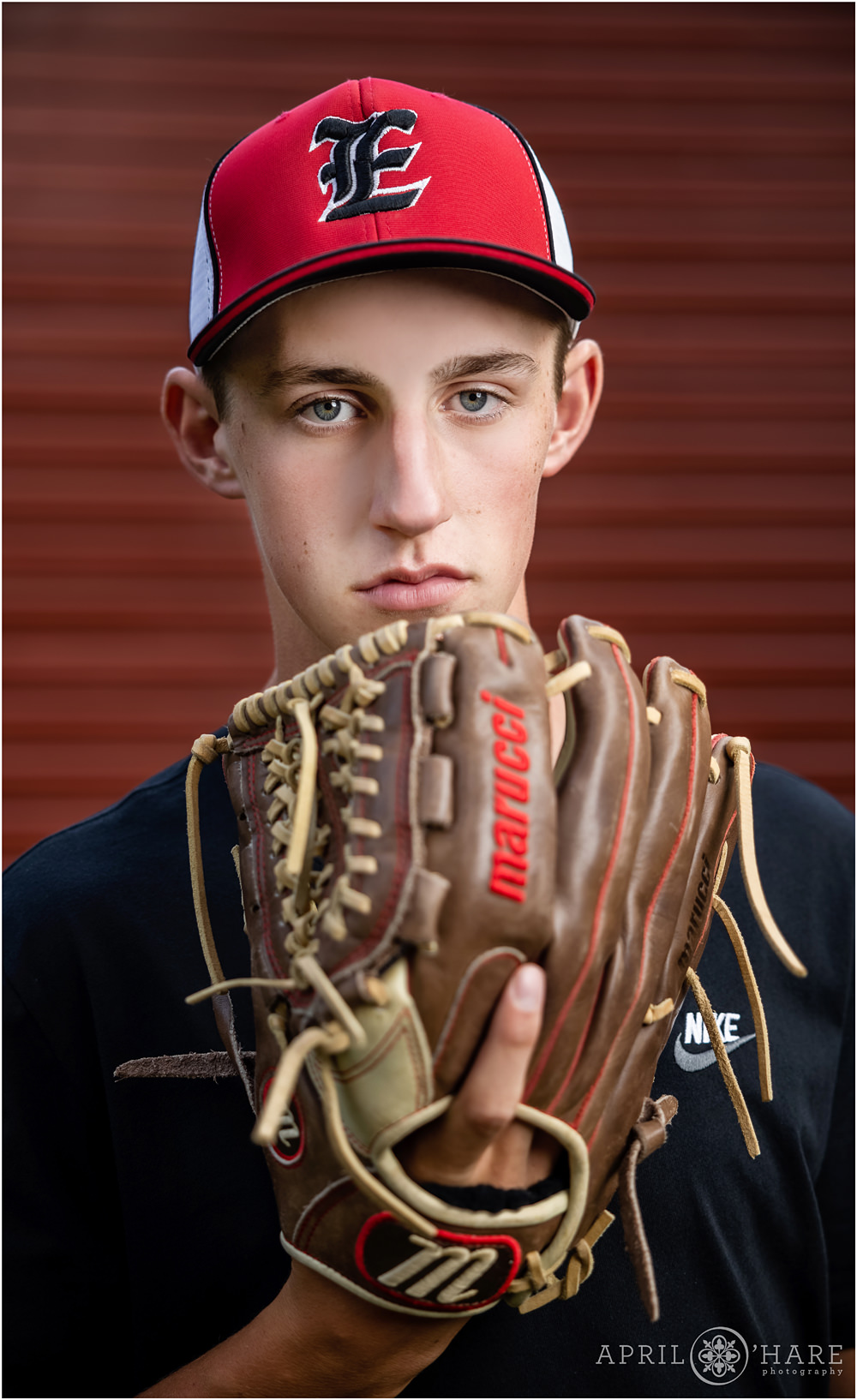 Serious Baseball Senior Photo with Mitt in front of Senior Boy's Face in front of red wall in Colorado