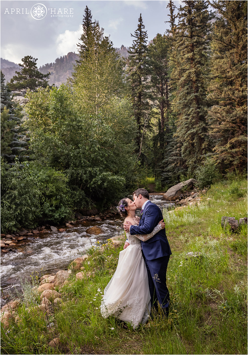Romantic portrait of Bride and Groom kissing in the wildflowers next to Fall River at Estes Park Condos