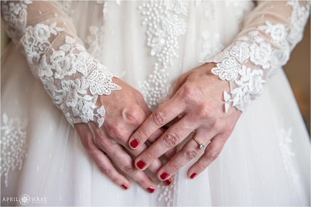 Detail photo of a bride's hands wearing her diamond engagement ring with painted red nails while wearing her wedding dress in Estes Park