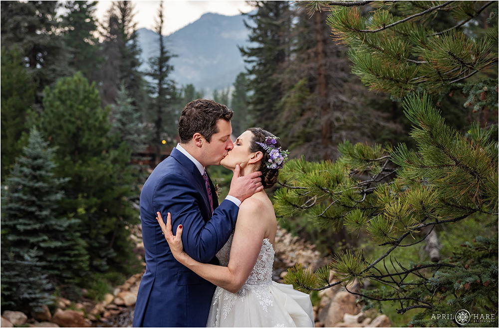 Sweet photo of a groom kissing his bride romantically in front of a beautiful mountain forest backdrop at Estes Park Condos