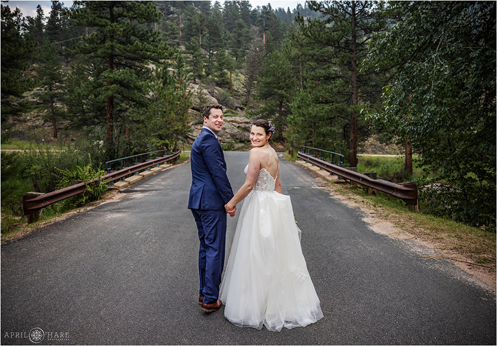 Bride and groom look back at the camera as they walk hand in hand down a road at Estes Park Condos