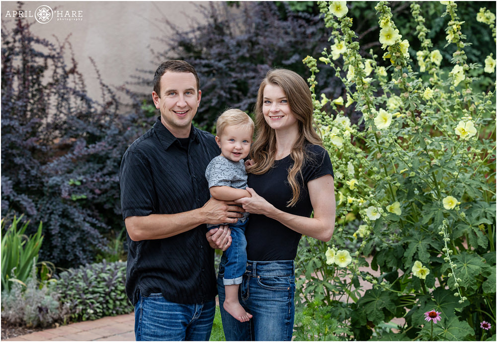 Family of 3 pose for a photo together with holly hock next to them at Denver Botanic Gardens