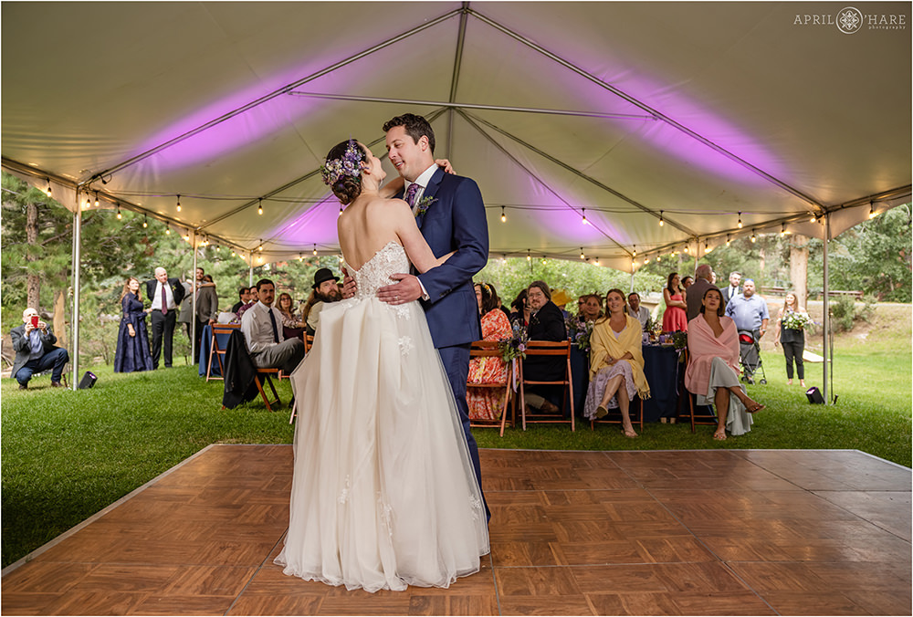 Bride with purple flowers in her hair dances with groom on a parquet wood floor in a white tent on the lawn at Estes Park Condos