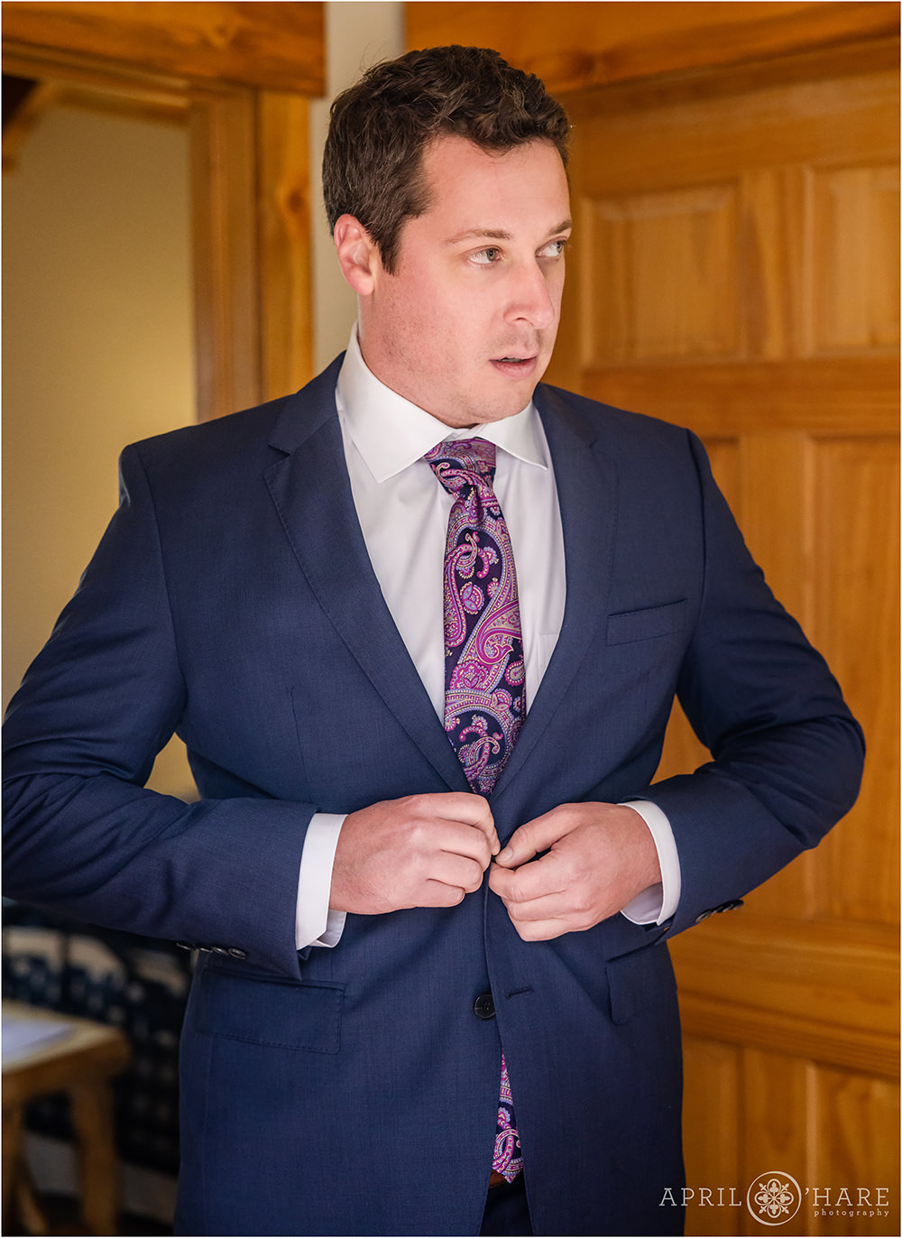 Tall groom with dark hair buttons his navy blue suit jacket inside the Estes Park Condos in Colorado