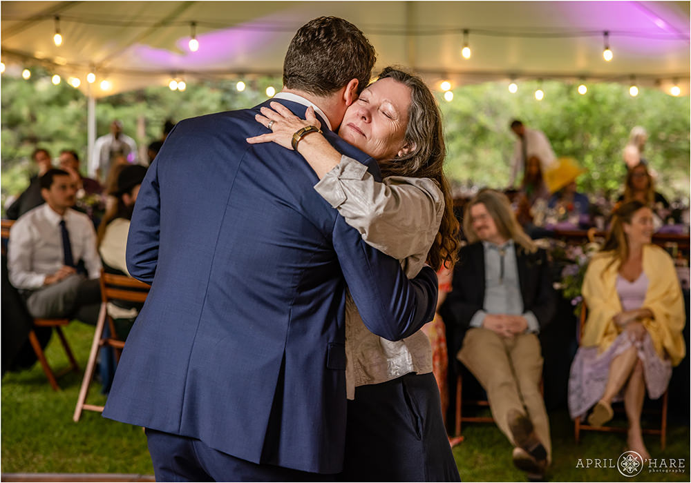 Groom and his mom hug during the Mother Son Dance at his outdoor wedding reception under a white tent in Estes Park
