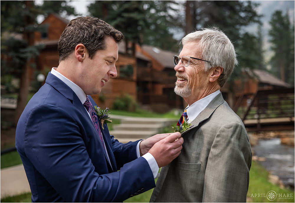 Groom helps his dad with his boutonniere next to Fall River in Estes Park