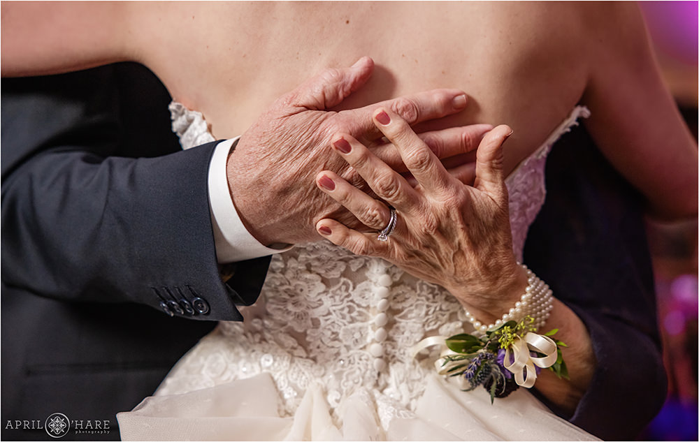 Detail photo of bride's parents hands as they hug their daughter on the dance floor at her Colorado wedding