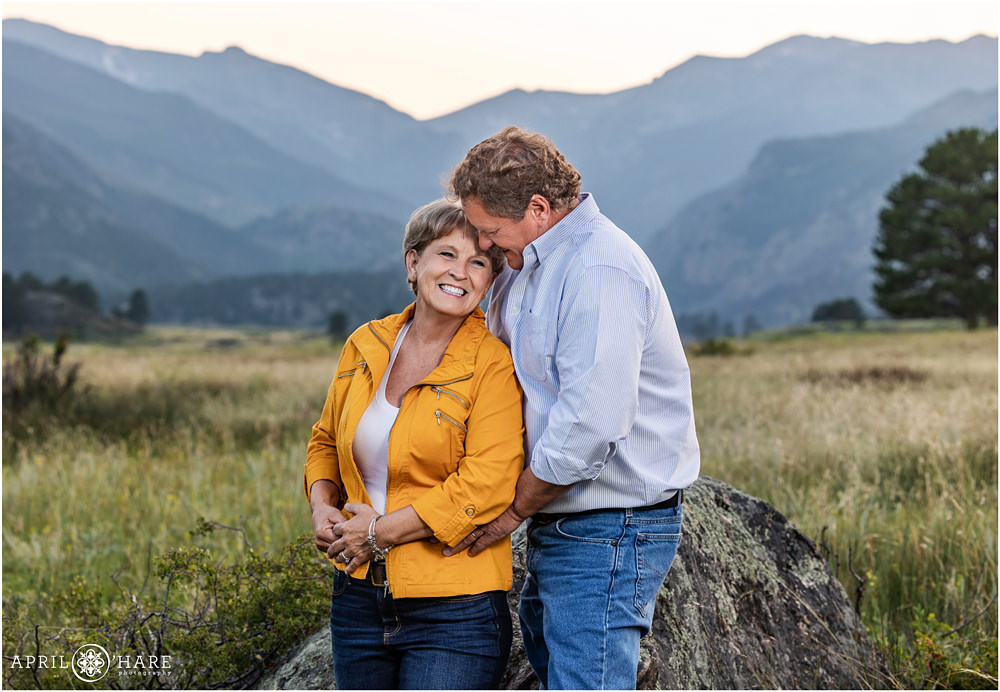 A sweet photo of a couple laughing together at their extended family portrait session with pretty blue mountain backdrop at Rocky Mountain National Park