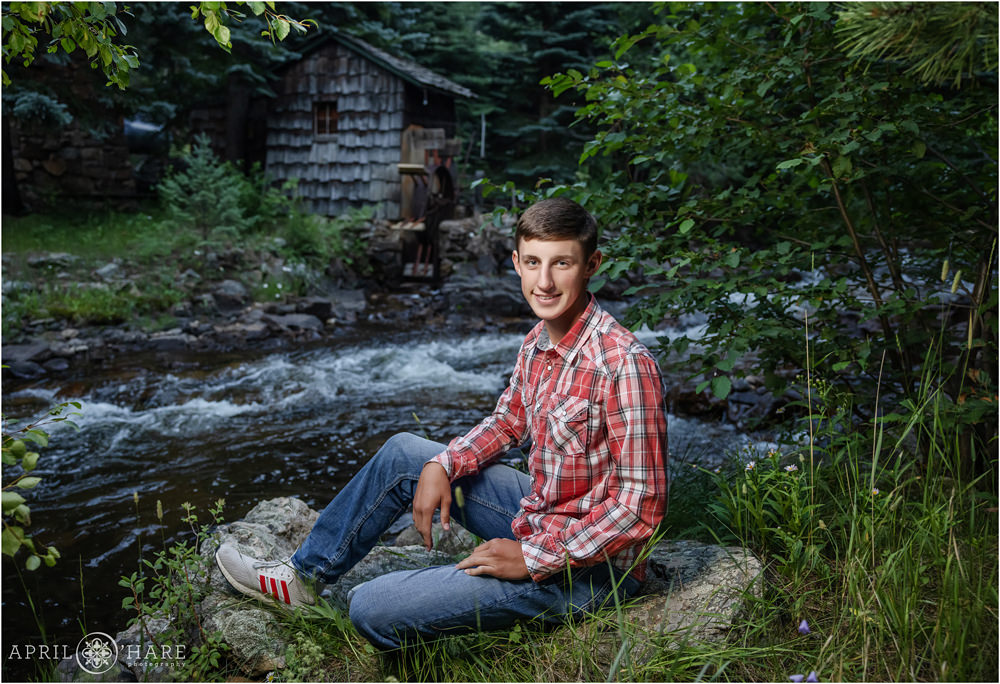High school senior boy in a rustic setting with mountain stream backdrop in Boulder Colorado