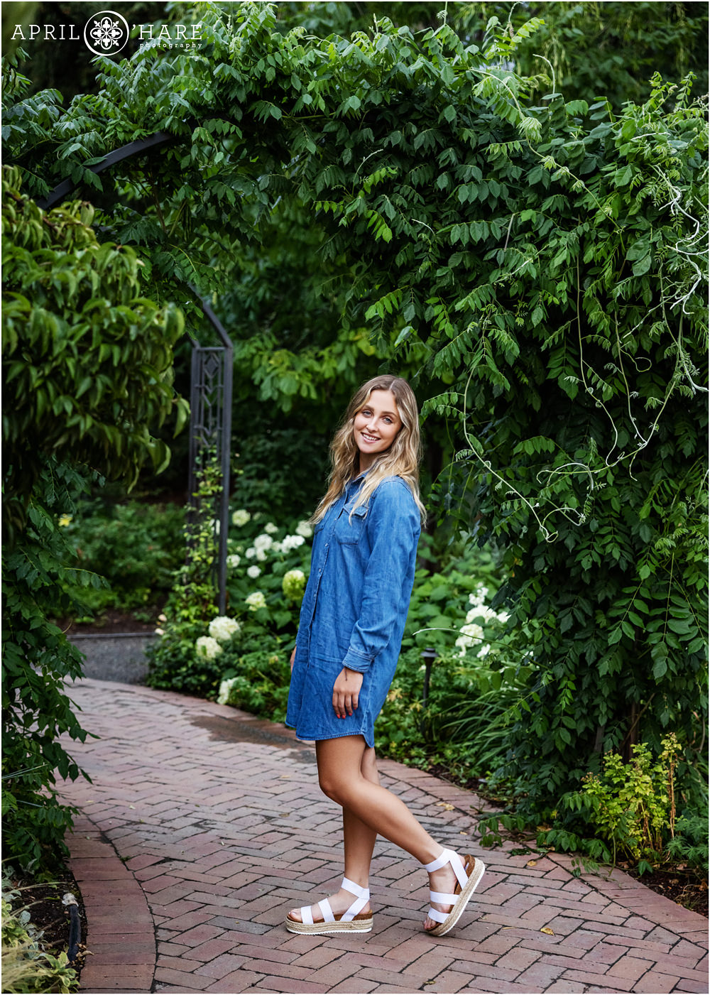 A senior girl wearing a blue chambray shirtdress with a green archway at Denver Botanic Gardens in Colorado