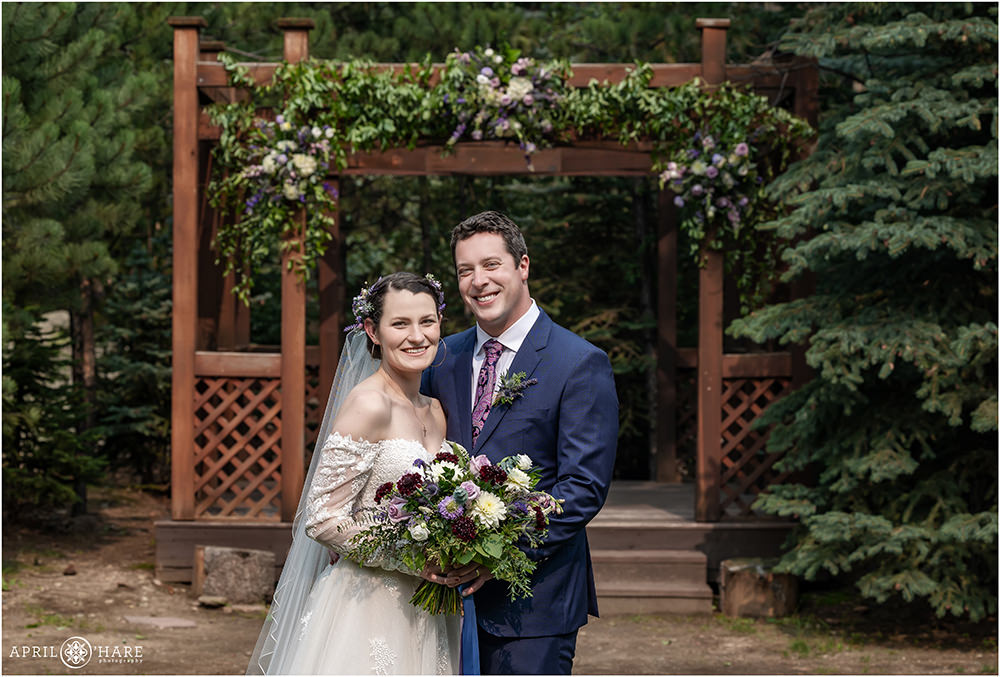 Classic wedding portrait of Bride and Groom smiling in front of their gazebo that's been decorated with Purple florals from Best Day Floral at Estes Park Condos