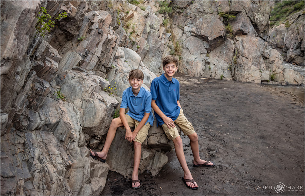 Twin boys wearing blue shirts and khaki shorts and leather sandals pose in front of a rocky backdrop at Viestenz-Smith Mountain Park for their birthday pictures