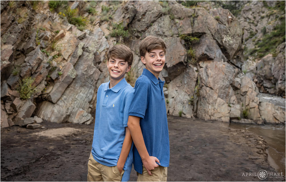 Twin teen boys earing blue shirts stand back to back next to the river at Viestenz-Smith Mountain Park in Loveland Colorado