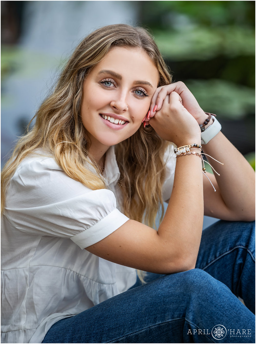 Senior girl wearing a white short sleeve blouse and jeans poses for her senior portrait in front of the waterlily garden at Denver Botanic Gardens