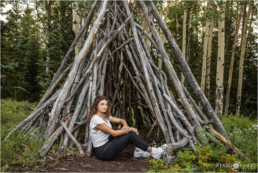 Cute girl poses with the fun wood log tipi structure in the woods of Evergreen Colorado