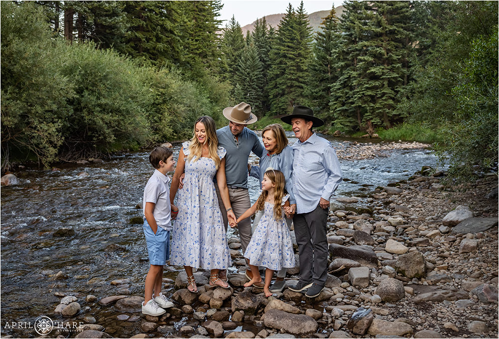 Family of six wearing white and blue with hats from Kemo Sabe pose next to Gore Creek in Vail Colorado