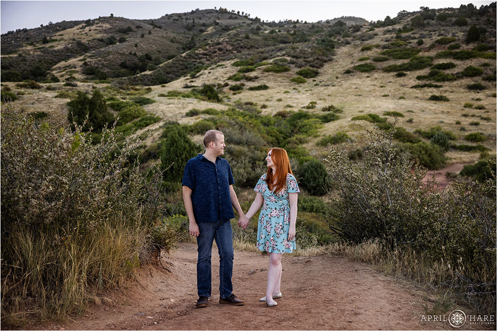 A cute redhead wearing a short blue floral summer dress holds hands with her fiance at their engagement session at East Mount Falcon Trailhead in Colorado