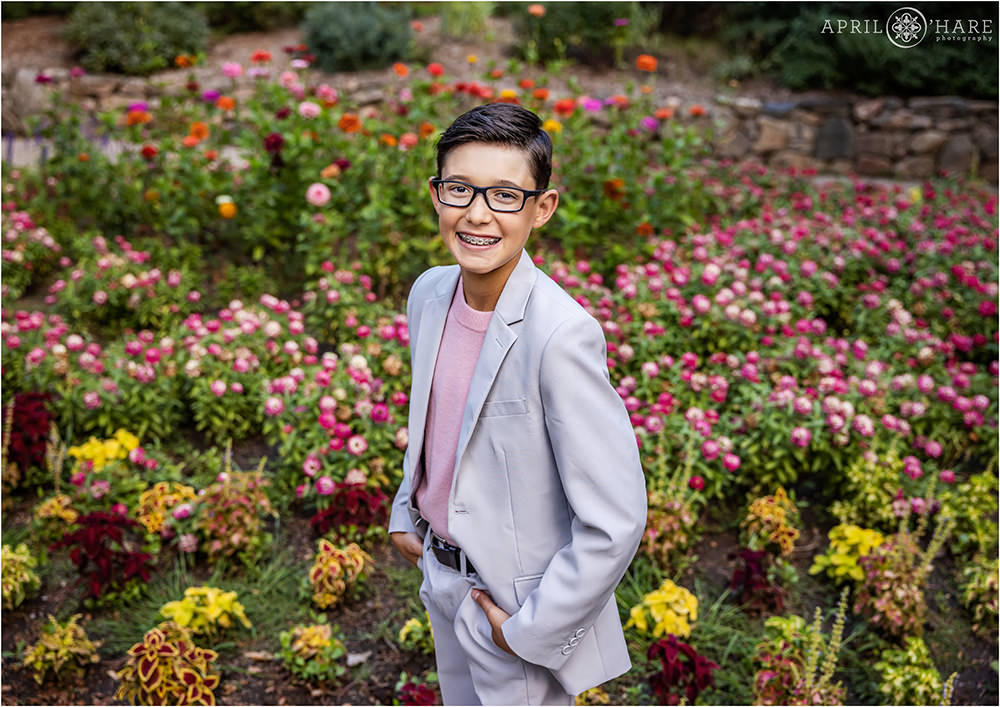 Dark haired tween wearing dark rimmed glasses, a light suit with pink sweater poses at his family's photography session in the Zinnia garden at Gallup Gardens in Littleton Colorado