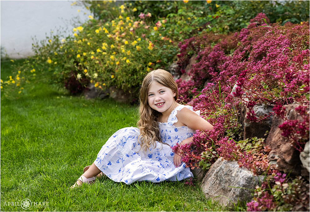 A cute girl wearing a white summer sundress with blue flowers on it poses in the garden at Interfaith Chapel in Vail