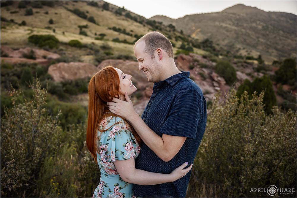 A man wearing a short sleeve button down shirt romantically holds his fiance's face and gazes into her eyes at their engagement photo session at East Mount Falcon