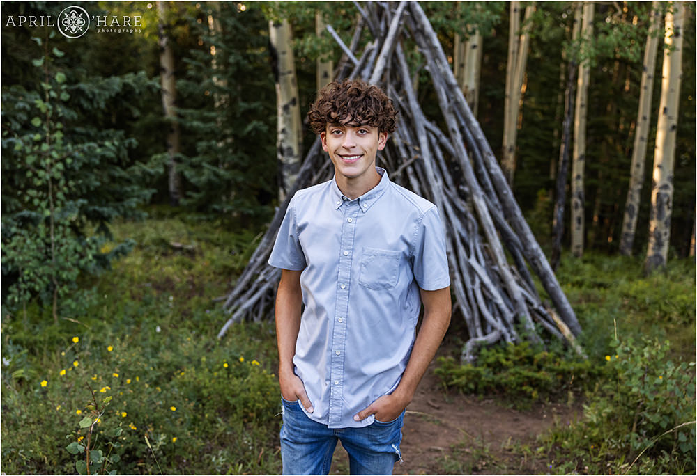 High school yearbook photo for a boy with curly brown hair wearing jeans and a light blue short sleeved button down shirt in the woods of Colorado