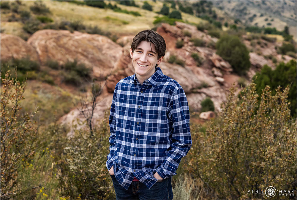 A high school senior guy with a natural smile on his face wearing a blue and white plaid button up shirt at the Mount Falcon East trailhead area in Morrison Colorado
