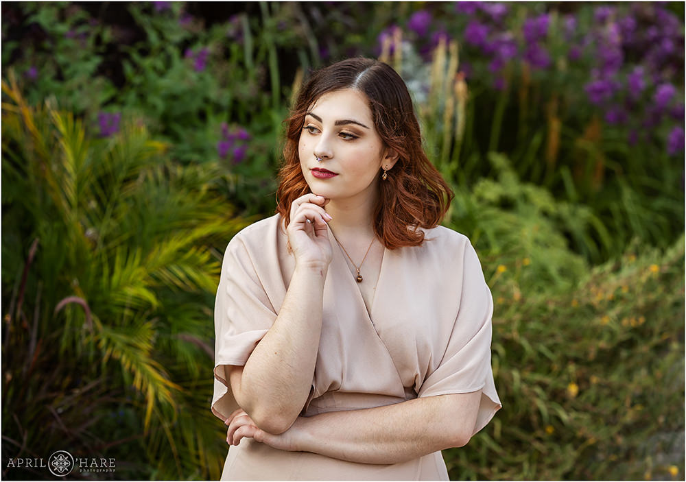 Young woman wearing a light pink dress and gold necklace poses in front of pretty purple flowers at Denver Botanic Gardens