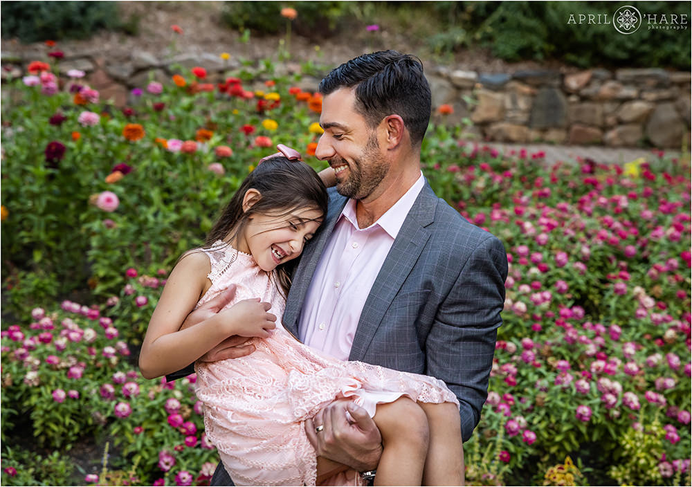 A dad holds his daughter, both wearing light pink as they laugh together at Gallup Gardens in Littleton