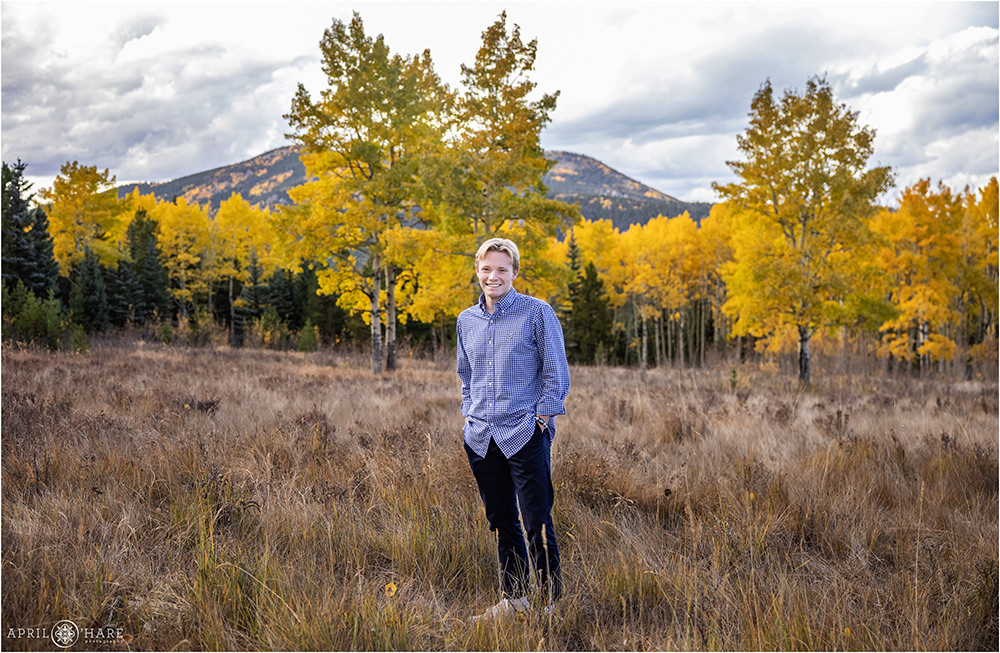 High school senior boy wearing a blue and white checkered button down shirt in a mountain meadow full of golden aspen trees in Colorado