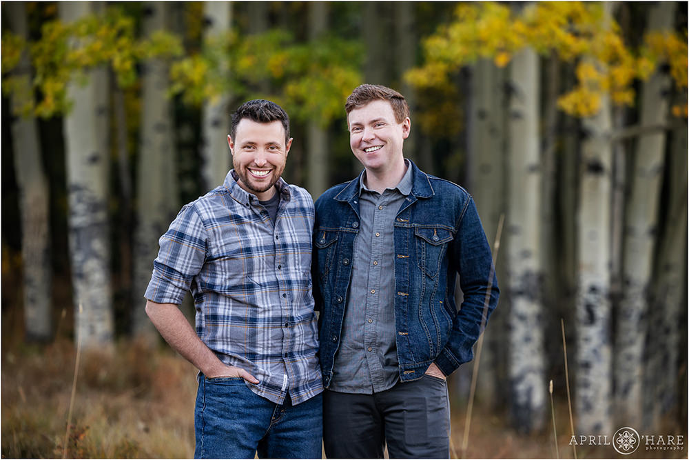 Two adult brothers wearing blue stand in an aspen tree forest together during autumn in Colorado