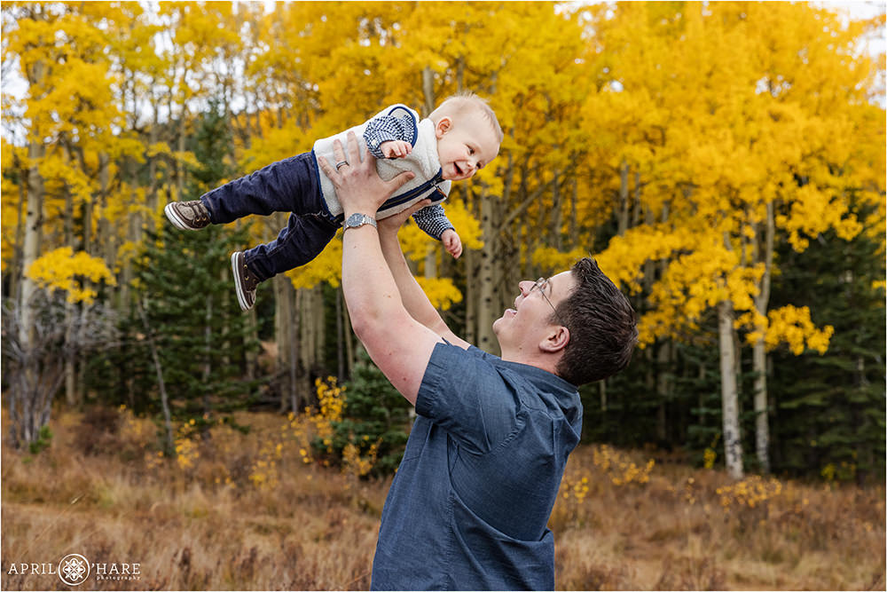Dad swings his 8 months baby in the air during fall color season in Evergreen CO